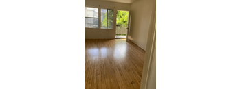 A room with wooden flooring and a view of a balcony through a doorway.