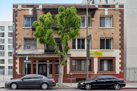 Two cars parked in front of a building with a tree in between.