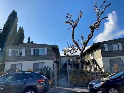A grey car is parked in front of a house with a tree in front of the house.