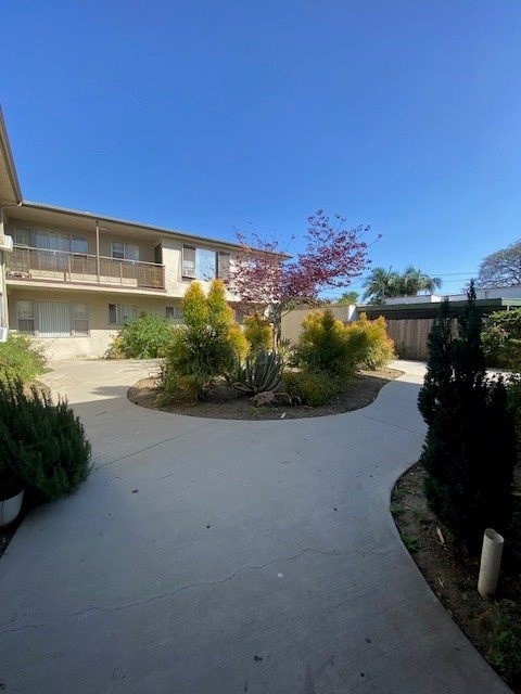 A concrete pathway leads to a two-story apartment building with a balcony.