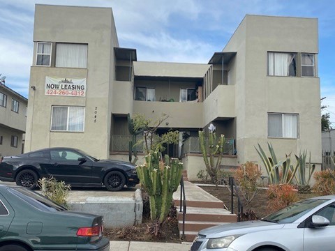 A building with a sign that says "NOW LEASING" is surrounded by parked cars.