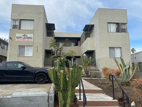A black car is parked in front of a building with a sign that says "NOW LEASING" and a phone number.
