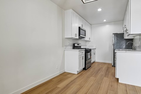 A kitchen with white cabinets and wooden floors.