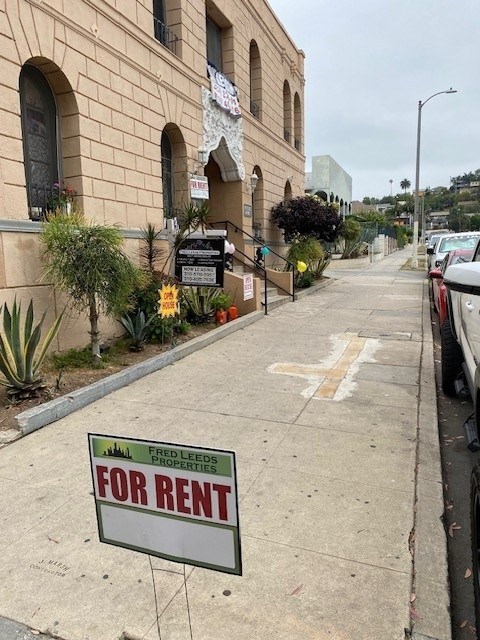 A sign for a property for rent is displayed on a sidewalk.