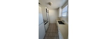 A kitchen with a white fridge, white cabinets, and a white sink.