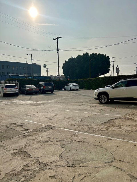A parking lot with a white car in the foreground and a building in the background.