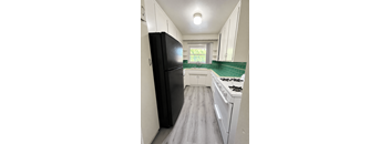 A black refrigerator stands in a kitchen with white cabinets and a green backsplash.