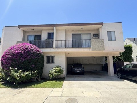A white two-story house with a balcony and a car parked in the driveway.