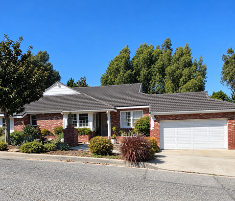 A house with a white garage door is surrounded by greenery.