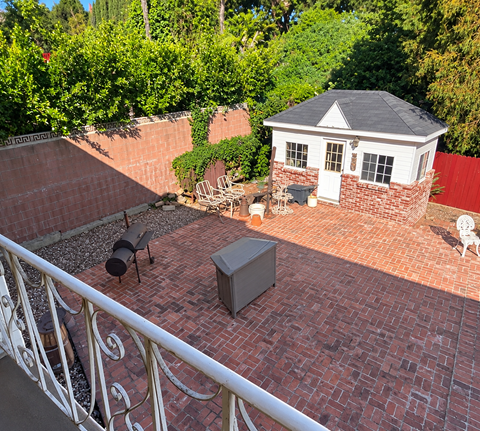 A small white house with a black roof is surrounded by a red brick patio and a white railing.