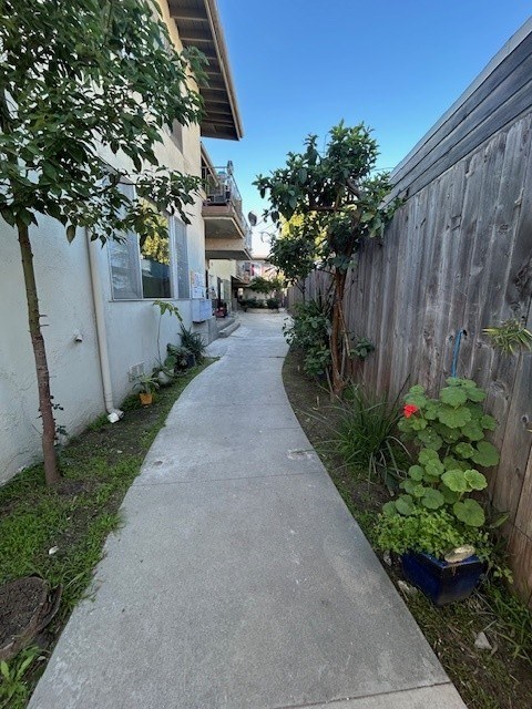 A narrow sidewalk runs between a white building and a wooden fence.