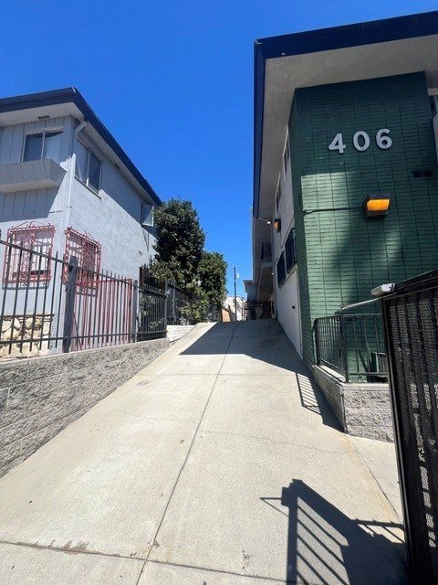 A sidewalk leads to a green building with the number 406 on it.