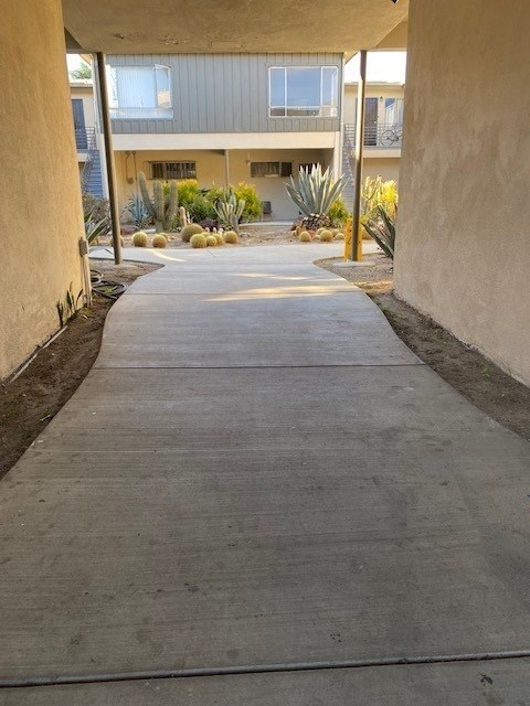 A concrete pathway leads to a building with a yellow pole on the right side.