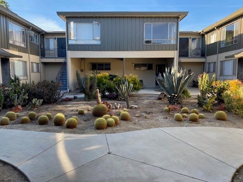 A concrete walkway leads to a two-story building with a balcony.