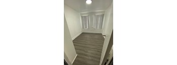 A room with wooden flooring and two windows with blinds.