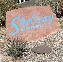 A sign that says Shellray Apartments is sitting in front of some grass.