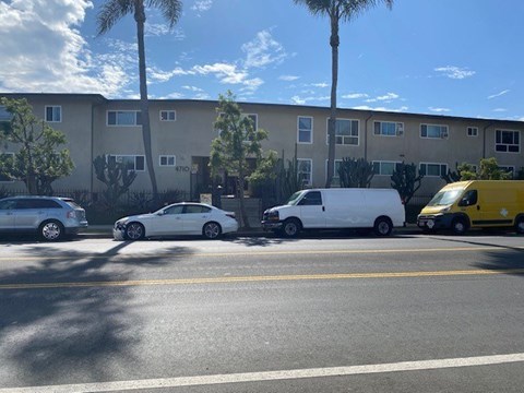 A white car is parked on the side of the road in front of a building with a yellow van and a white van parked behind it.