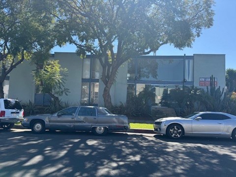 Two cars parked in front of a building with trees in the background.