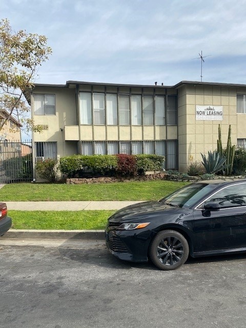 A black car is parked in front of a building with a sign that says "NOW LEASING".