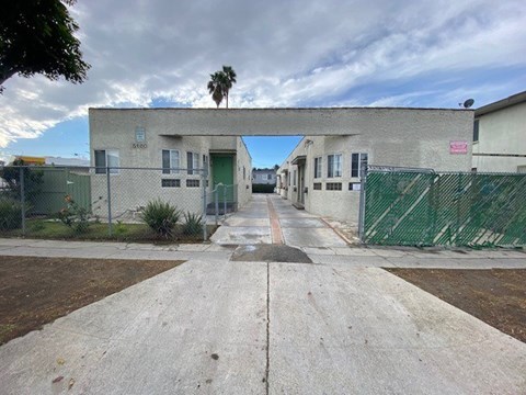 A concrete pathway leads to a building with a green fence on either side.