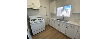 A white kitchen with a stove, sink, and cabinets.