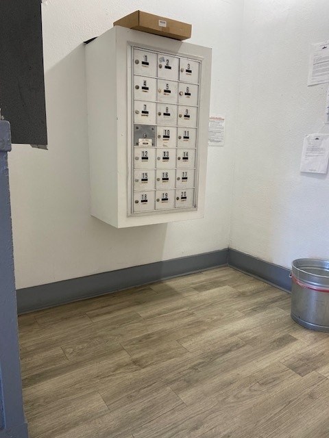 A metal bucket is on the floor next to a wall with a panel of switches.