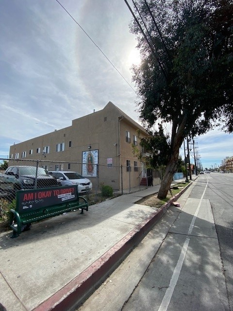 A street view with a building on the left and a bench with a sign on it.