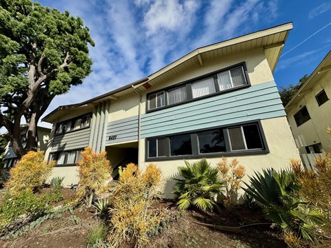 A house with a blue and beige exterior is surrounded by greenery.