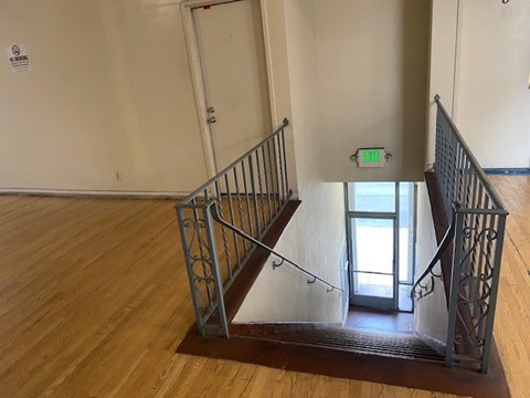 A staircase with a metal railing and wooden steps leading to a door with a green exit sign above it.