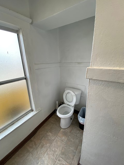 A white toilet is in a small bathroom next to a window.