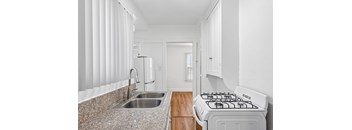 A kitchen with a stove, sink, and cabinets.