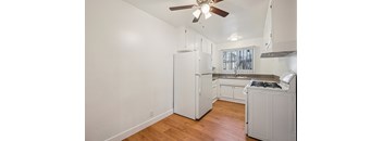 A white kitchen with a refrigerator, stove, and a ceiling fan.