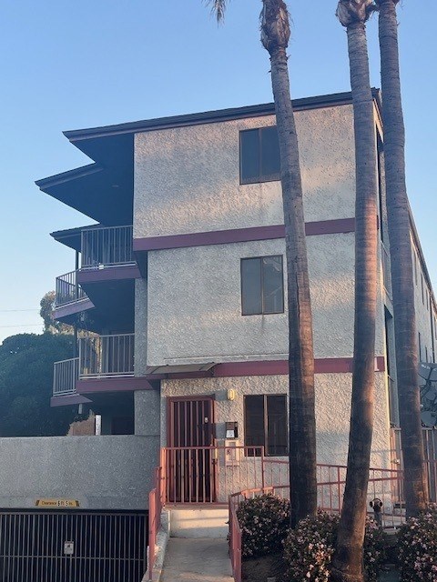 A two-story building with a balcony and palm trees in front.