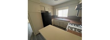 A kitchen with a black fridge, white countertop, and a window with blinds.