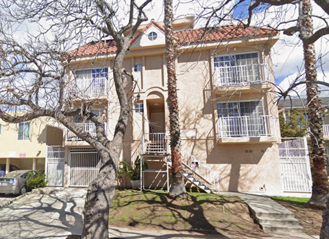 A beige two-story building with a red tile roof and a balcony on the second floor.
