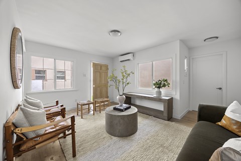 A living room with a brown sofa, a wooden chair, a round table, and a large mirror on the wall.