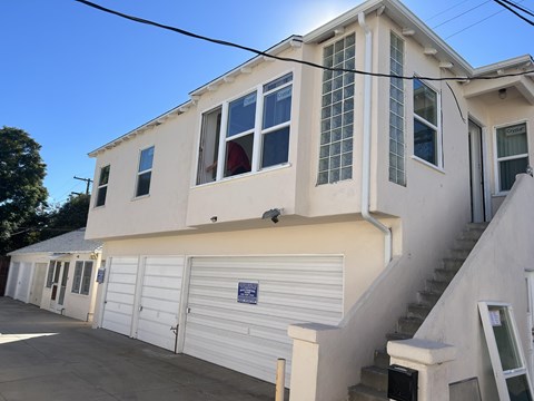 A white building with a garage door and a staircase leading to the second floor.