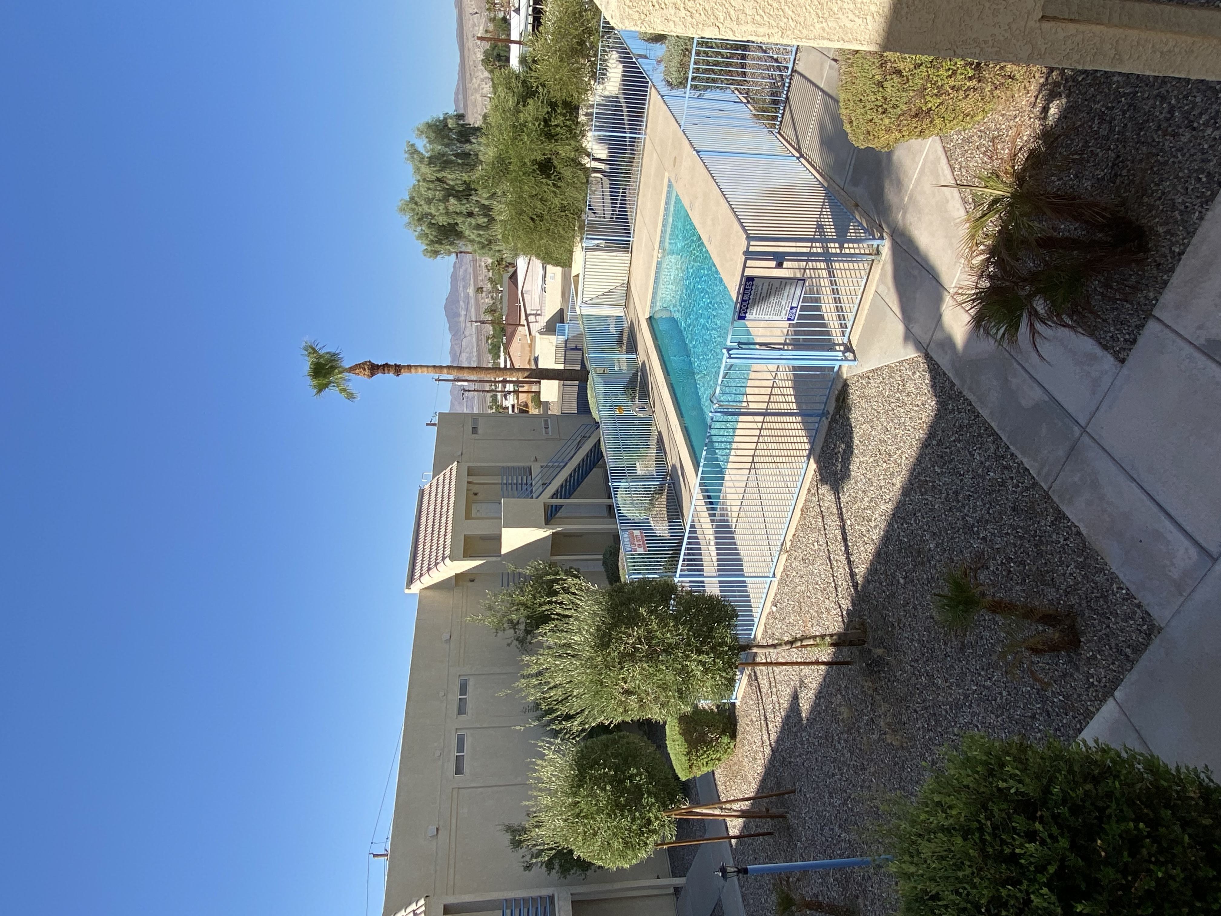 A swimming pool is surrounded by a concrete patio and a tall building.