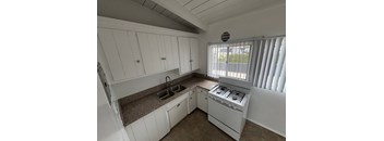 A white kitchen with a sink, stove, and cabinets.