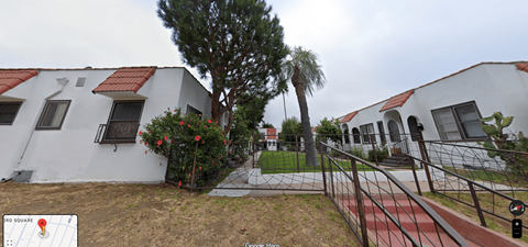 A white building with a red roof and a tree in front.