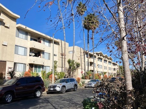 A row of apartment buildings with cars parked in front.