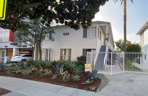 A house with the number 1232 on it is surrounded by a white fence and has a sign in front of it.