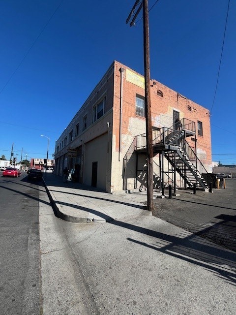 A red car is parked on the street in front of a brick building with a fire escape.