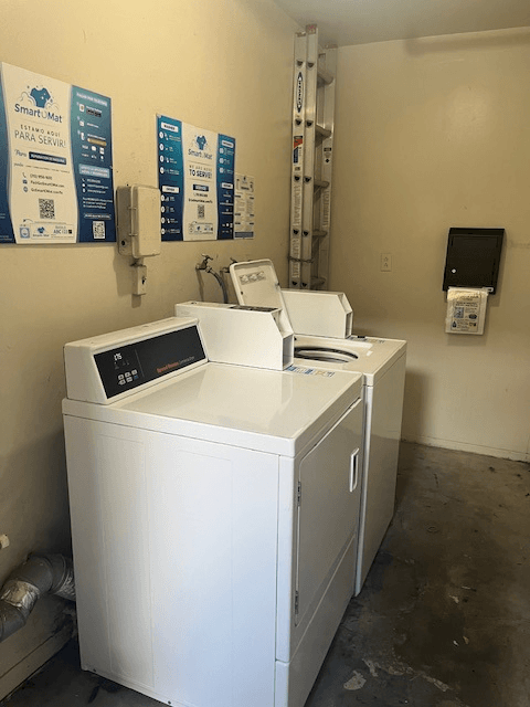 A white washing machine in a room with a wall-mounted monitor and a SmartMatic sign.