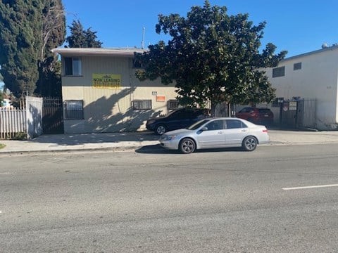 A car is parked in front of a building with a "Now Leasing Apartments" sign.