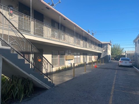 A car is parked on the street in front of a building with a balcony.