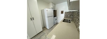 A kitchen with a white fridge and a stone backsplash.