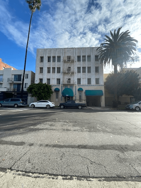 A white car is parked in front of a building with a blue awning.