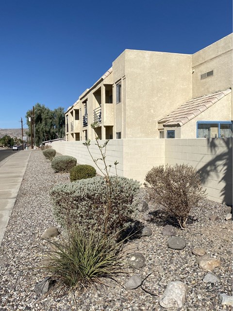 A building with a grey facade and a blue door is surrounded by a gravel garden.