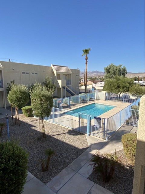 A pool surrounded by a fence and trees in a desert landscape.